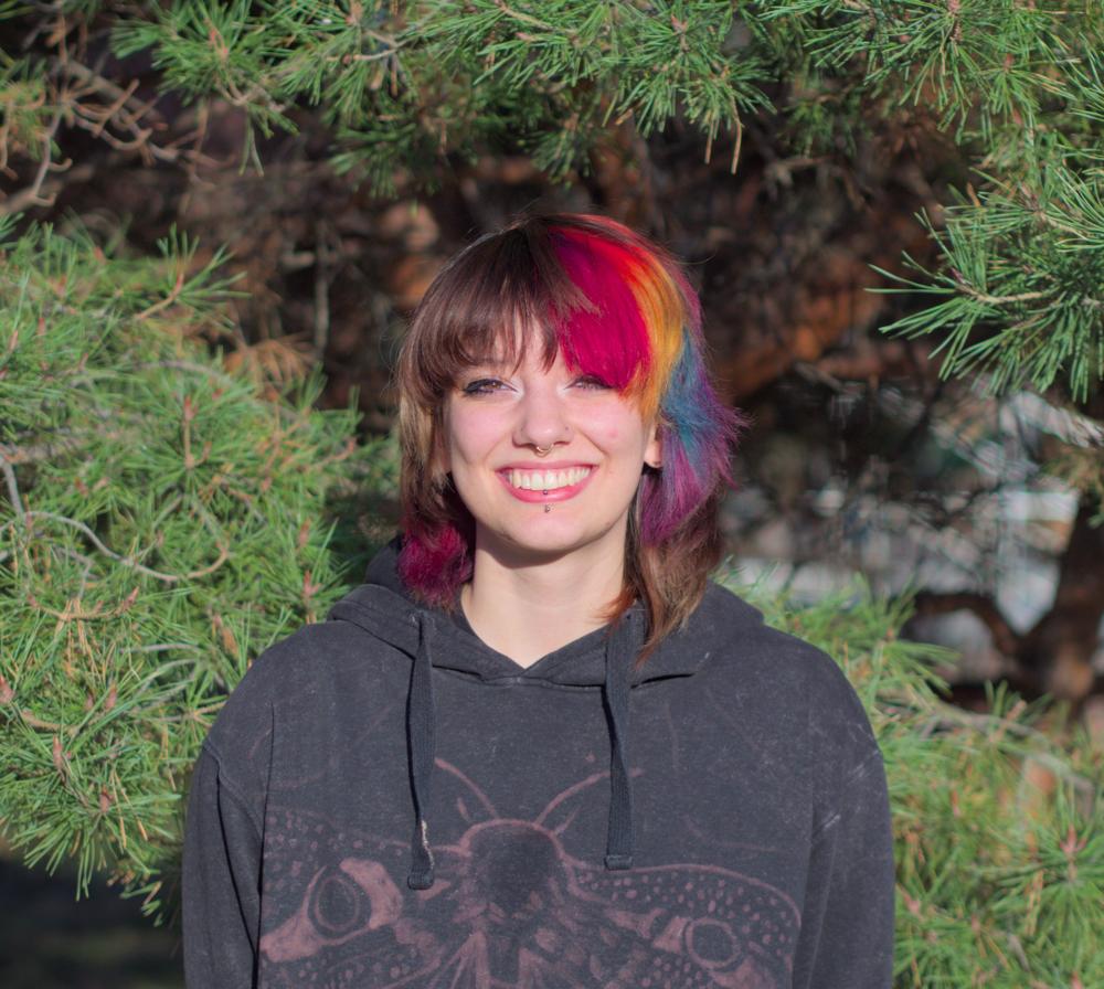 My partner who is a very cool looking person smiling with a natural green background