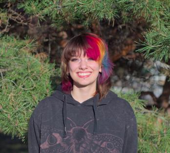My partner who is a very cool looking person smiling with a natural green background